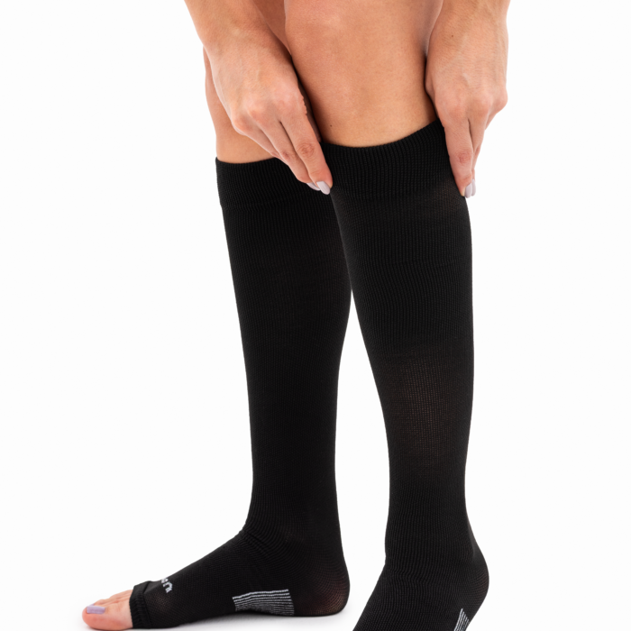 Modelo colocándose las medias antiembólicas a la rodilla Athlon TVP300 negras, destacando la compresión graduada y la puntera abierta.